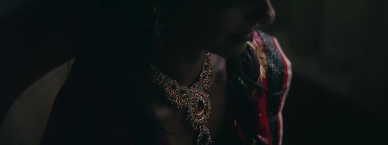 A man poses in an ornate gold necklace and embroidered sash