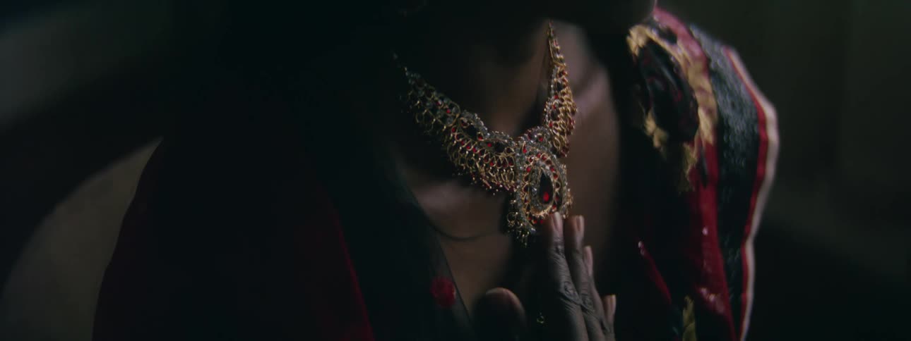 Young hindu woman sitting on a dimly lit room rubs a golden necklace with her hand