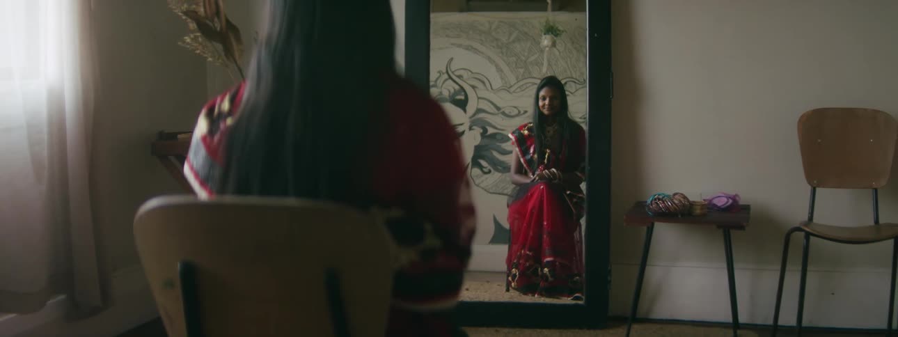 A woman sits in front of a mirror in a dress