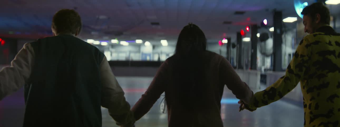 A young woman holds hands with two friends while skating in a roller rink