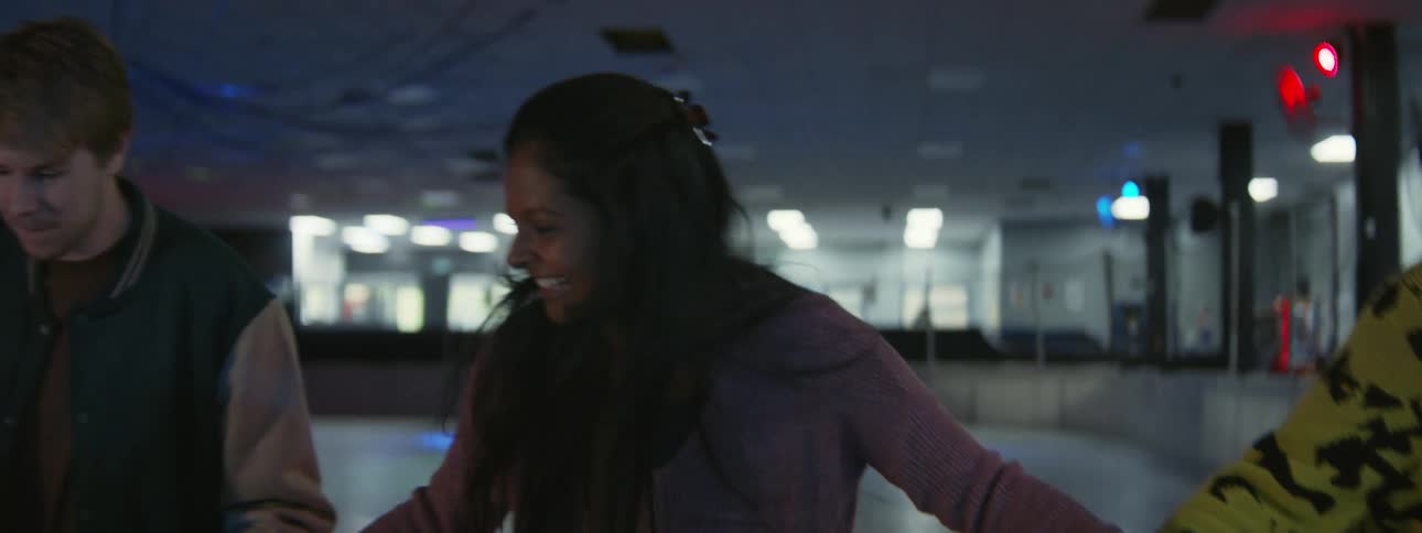 Group of happy friends smile while trying to keep balance while ice skating holding hands