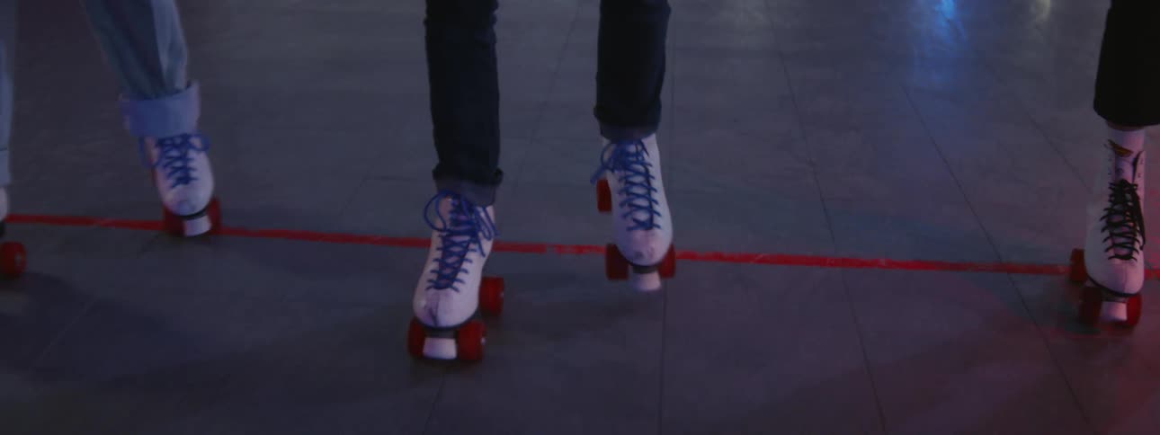 Three people wearing roller skates move together across floor reflecting lights