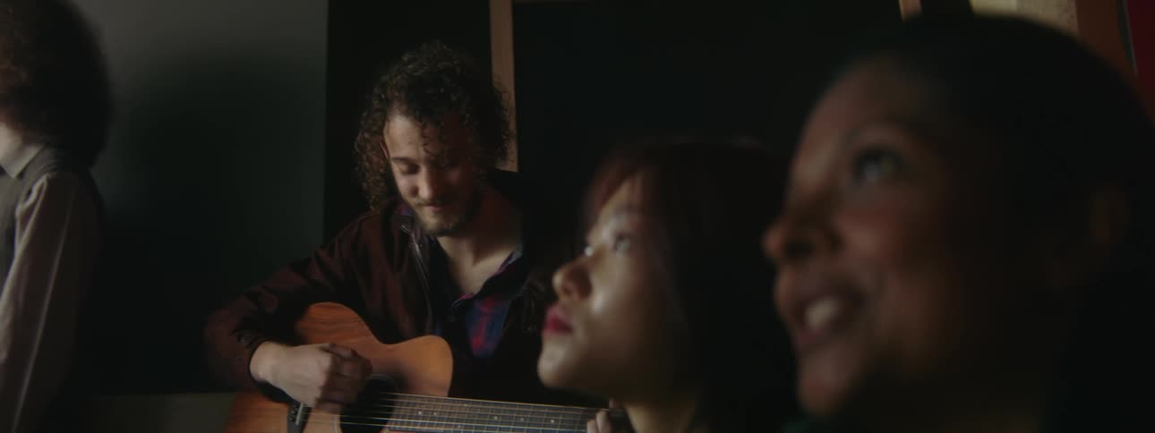 Two women singing while man plays the guitar in a group setting