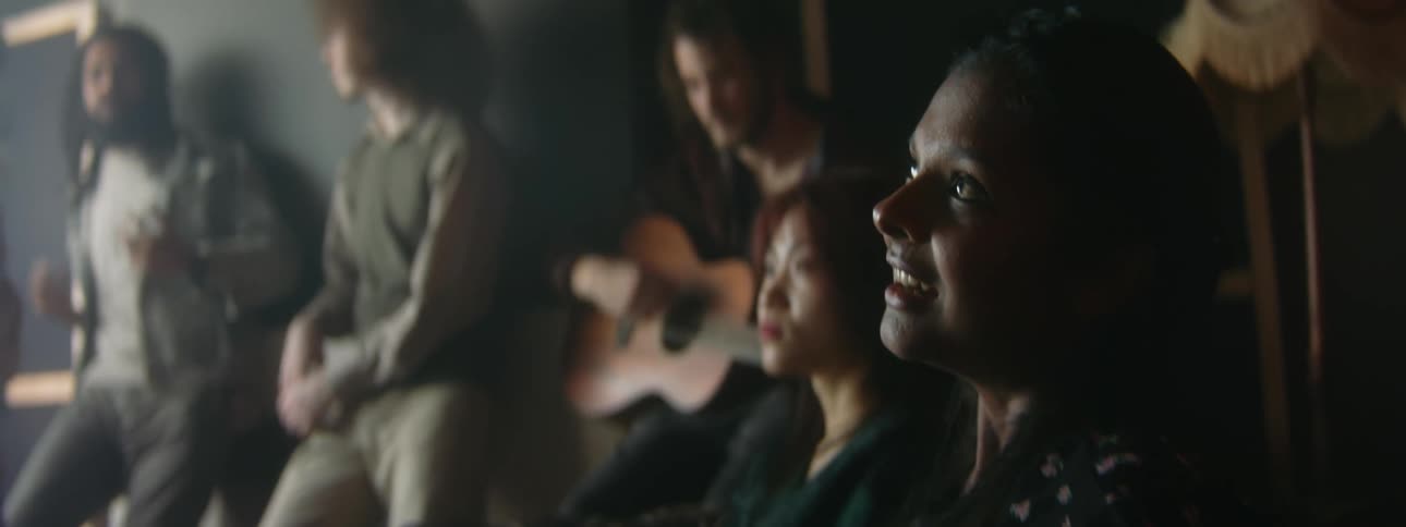 A woman sings as a man plays guitar in a room full of people