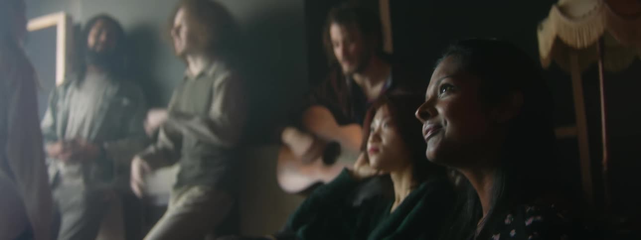 A man plays guitar as a group of people talks