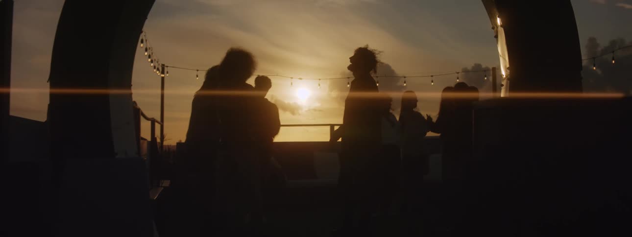 Silhouette of a group of friends having fun on a small party in the patio at sunse
