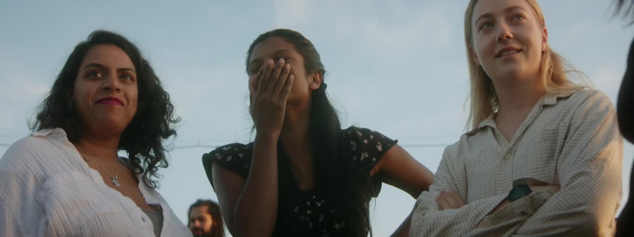 Woman covers her mouth with her hand as she laughs while standing with several other women outdoors