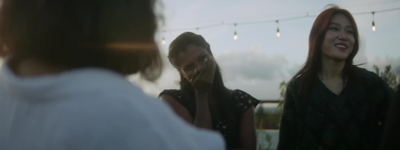 Woman covers her mouth with her hand as she laughs with several other women as they stand outdoors