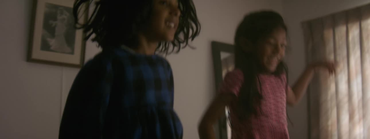 Sisters are jumping indoors in there room in the middle of the day