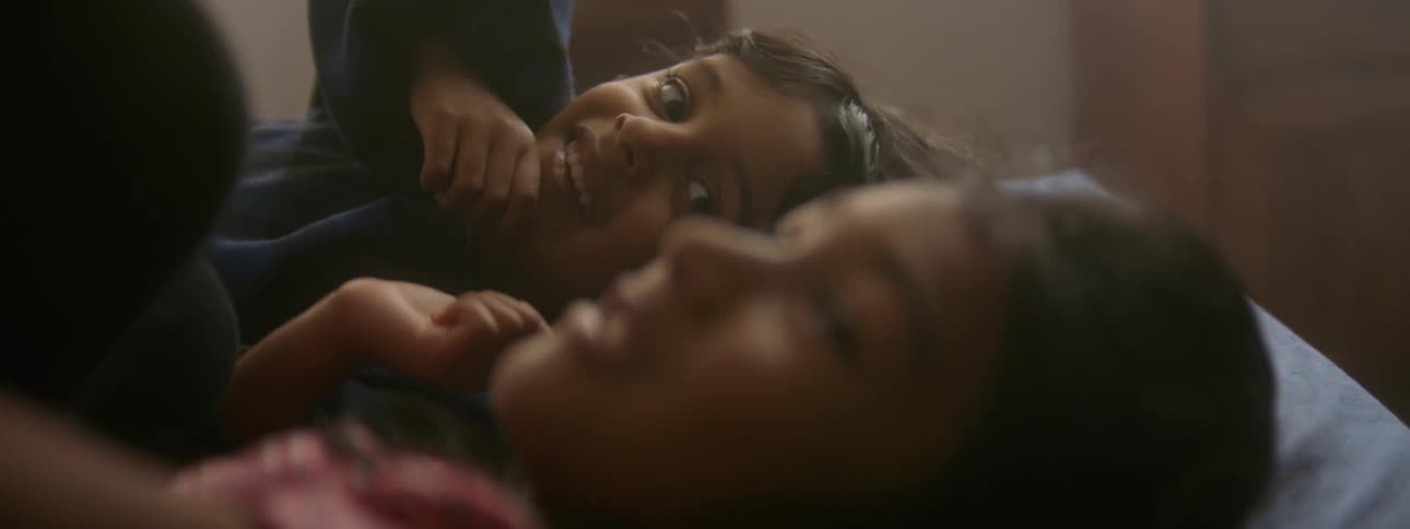Two sisters laugh and talk as they lay in bed