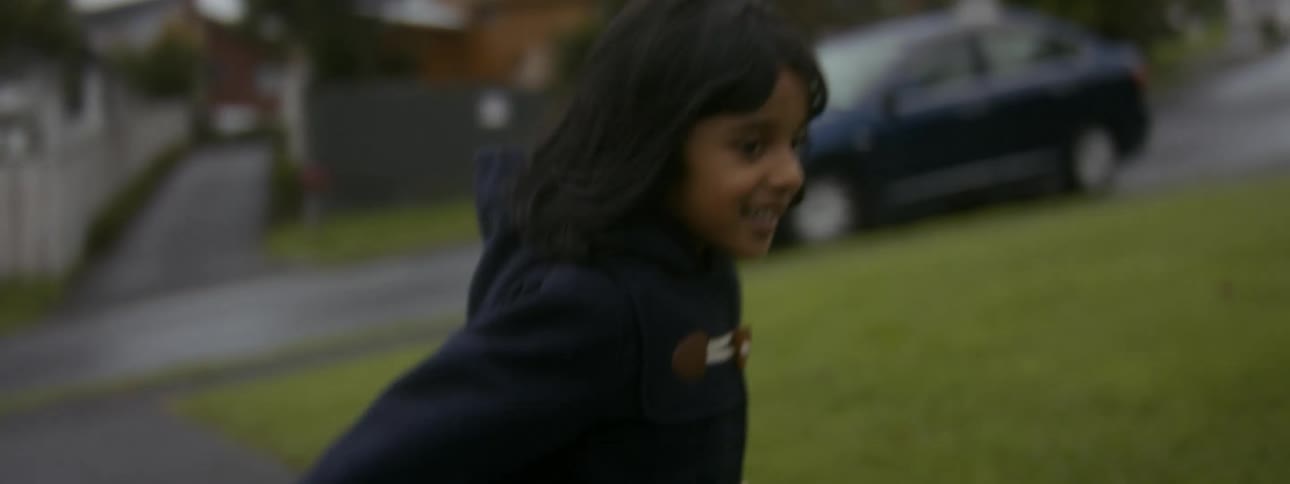 A young girl runs across a lawn in a neighborhood