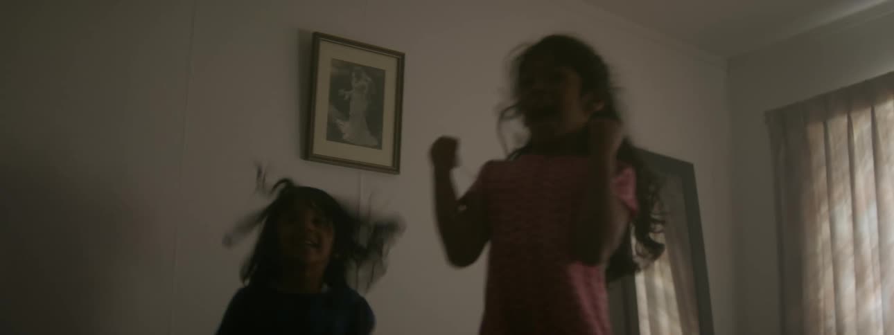 Two young girls are playing and jumping on a bed when somebody opens the door