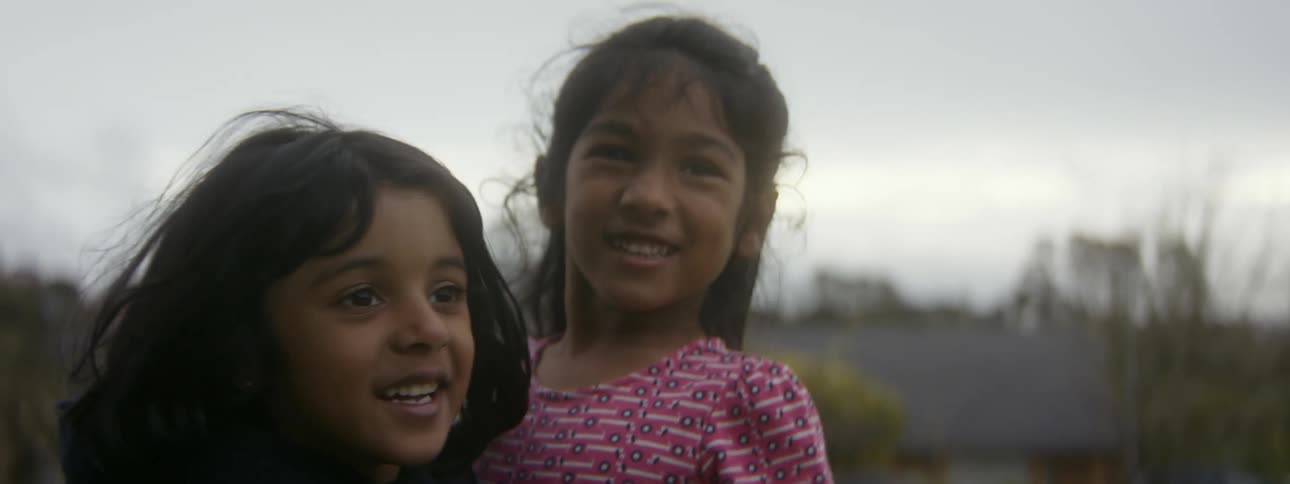 Two girls hugging and smiling outside on a cloudy day