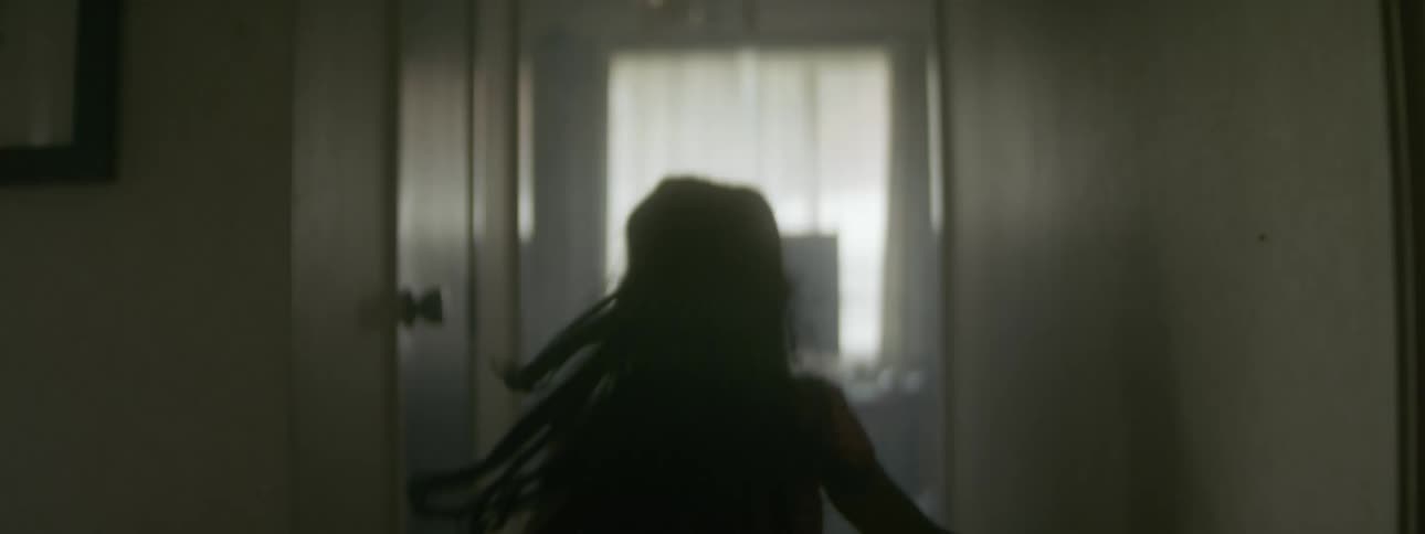 A little girl with long dark hair is running through a hallway into a room and her hair bounces as she runs