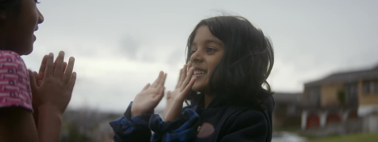 Two young girls are outside playing and clapping their hands together