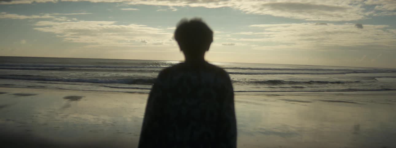 Woman stands silhouetted on beach looking out to sea