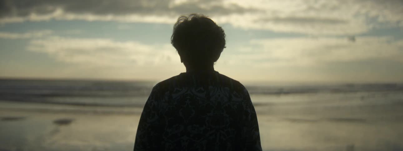 A woman standing facing the ocean waves deep in thought alone on the beach