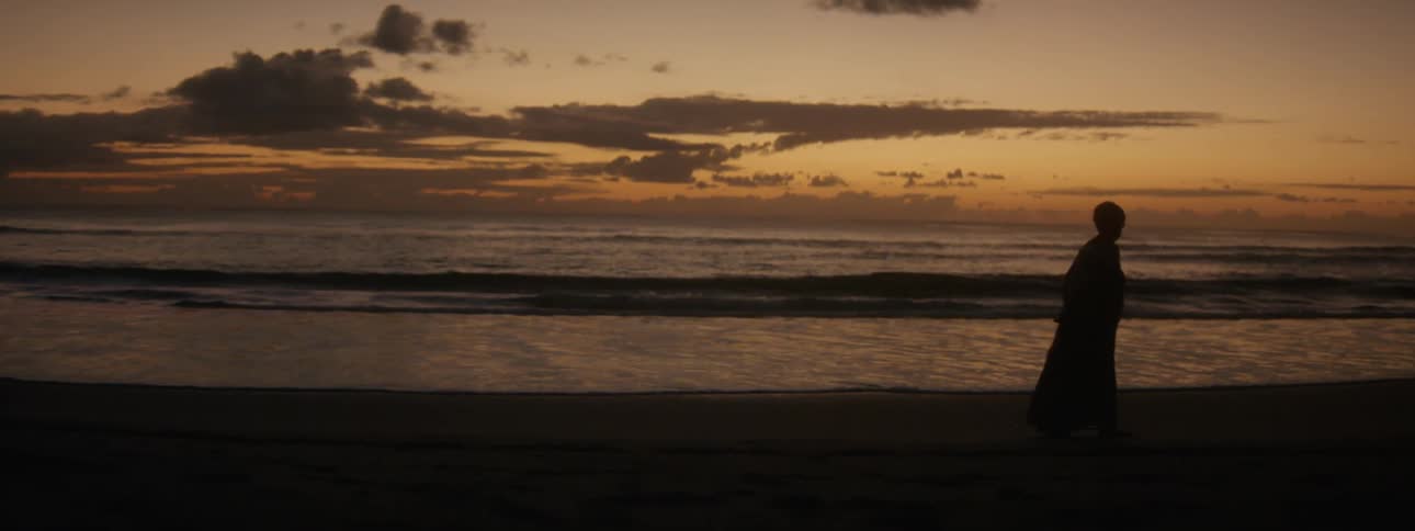 Woman walking across the beach as the surf comes in is silhouetted against the red sky on the horizon