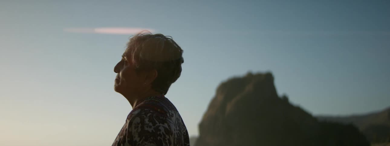 Woman stands against pale red tinted sky with rock outcropping in the background