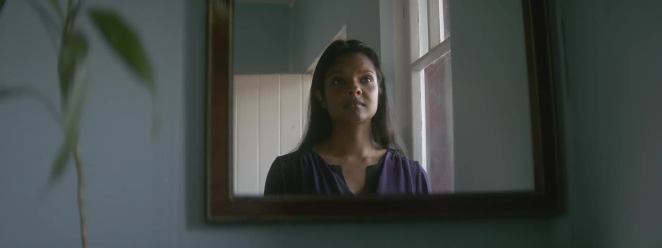 A woman is standing in a room near a window and she looks up