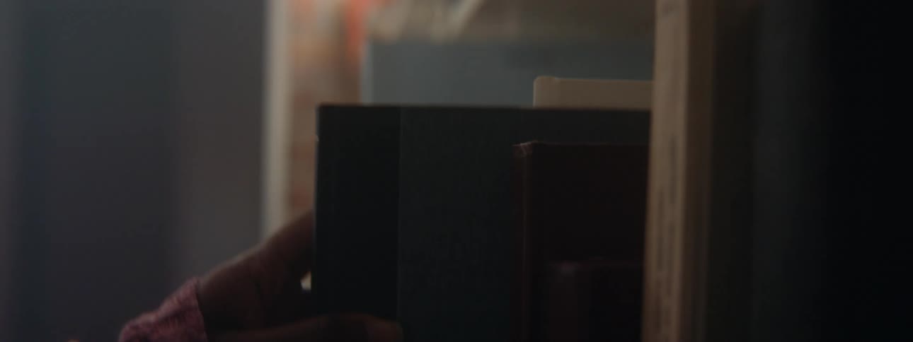 A persons hand is seen placing a book on a bookshelf next to other books in a library