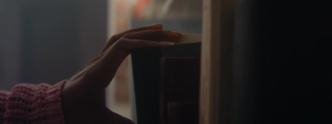 Girls hand with pink sweater puts book in bookcase