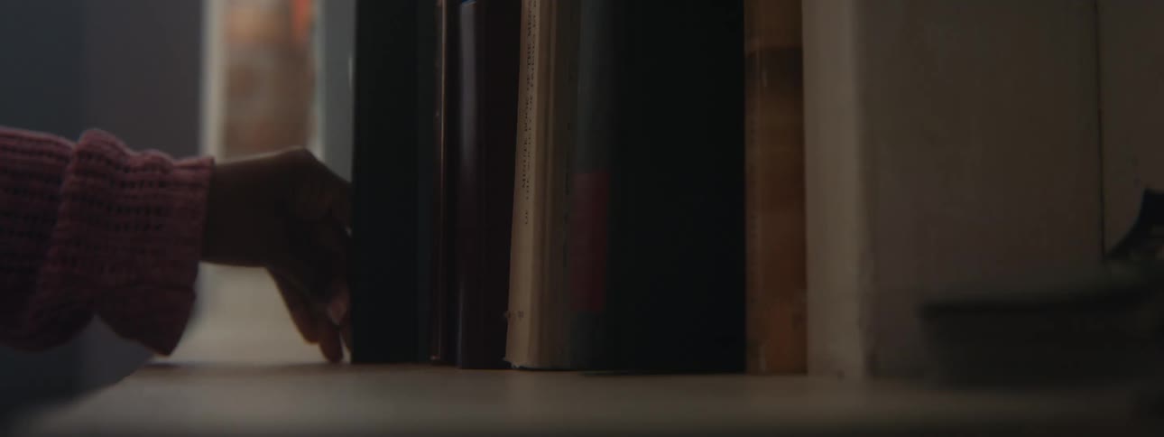 Girls hand with pink sweater puts book in bookcase