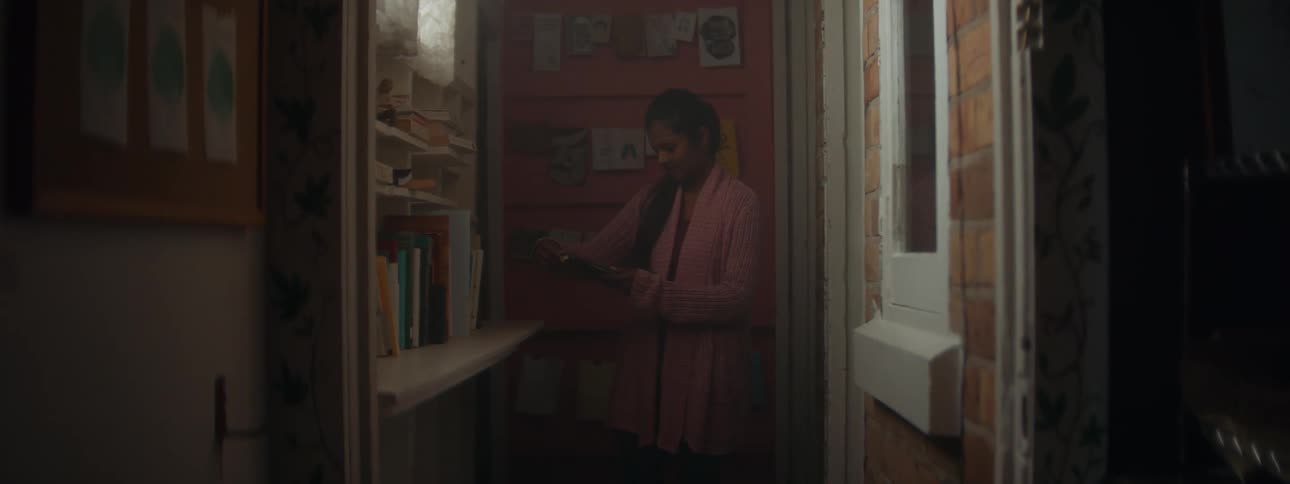 Woman with a ponytail and pink coat picks book from bookshelf