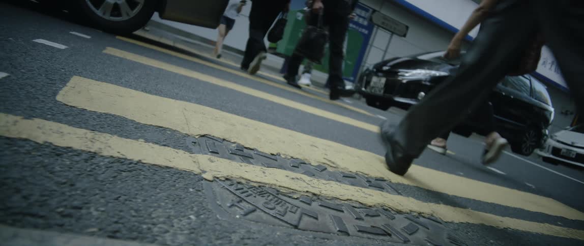 People are walking across a zebra crossing on a street near automobiles and toward a building