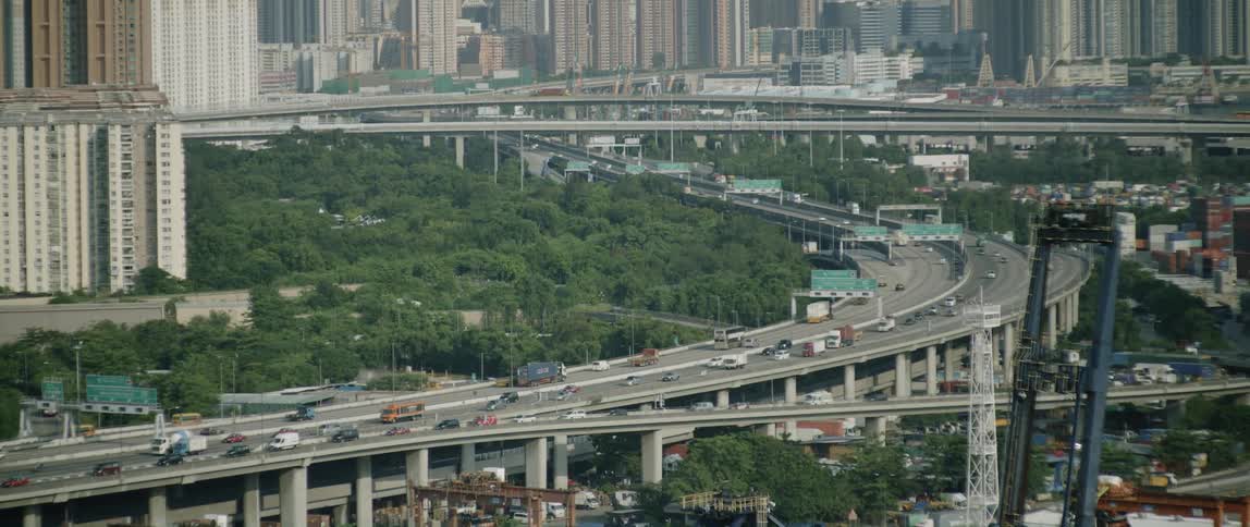 Countless vehicles traverse a curved freeway near a major metropolitan city