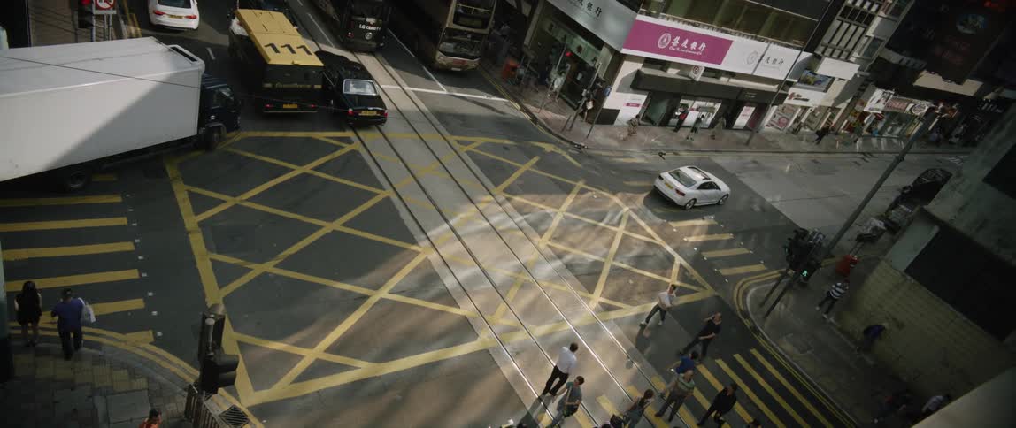 A white car passes through an intersection as pedestrians cross the street nearby