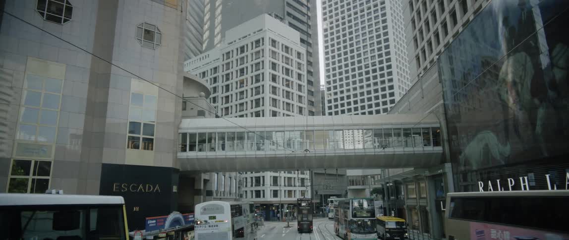 Buses and trolleys travel on a wide hong kong street lined with shops and buildings