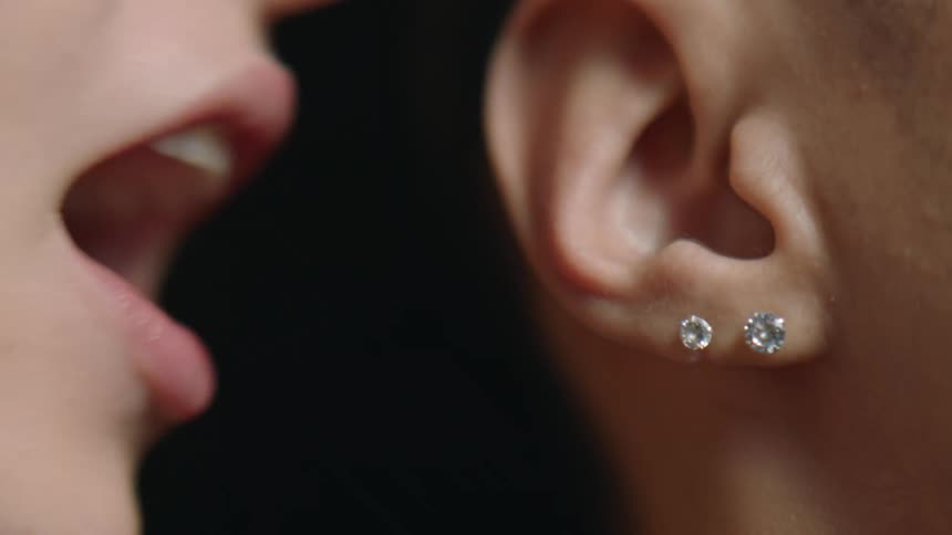 A woman whispers directly into a mans ear