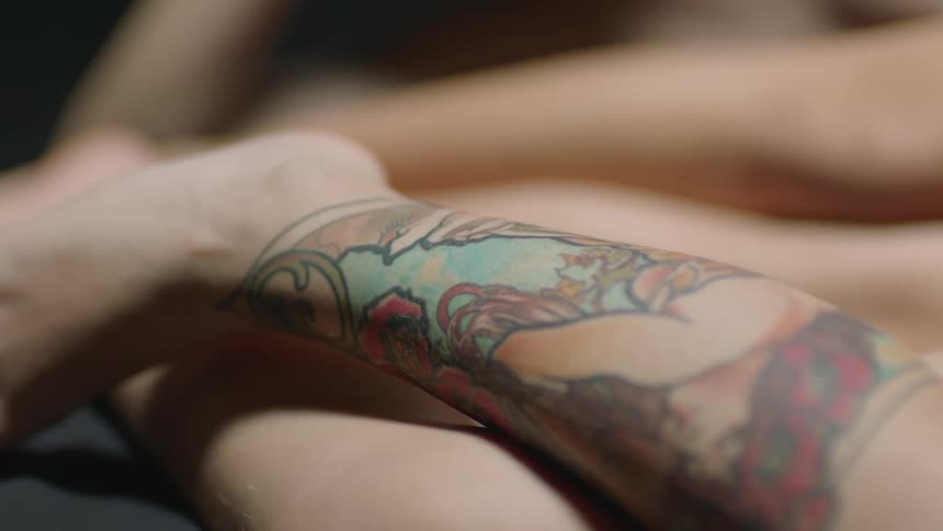 A person with their leg tattooed lays next to another person