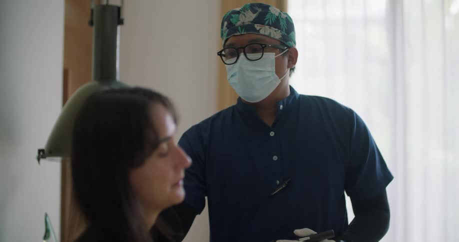 A woman is sitting up in a hospital bed and a doctor is holding an instrument as he speaks to her