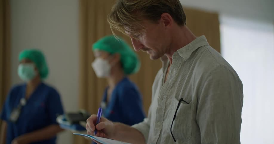 A man reviews a chart while a doctor and nurse chat behind him