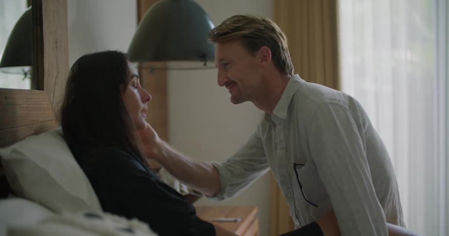 A man checks his wifes temperature while she lies in bed