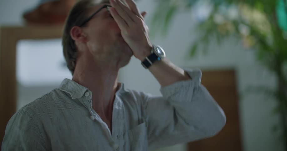 A man at home looks at a bottle of pills and puts some in his hand and then his mouth and takes a drink of water