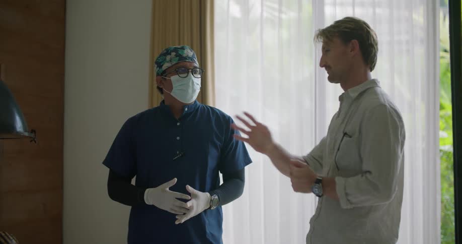 A man gestures with his hands as he talks with a doctor in front of sliding glass doors