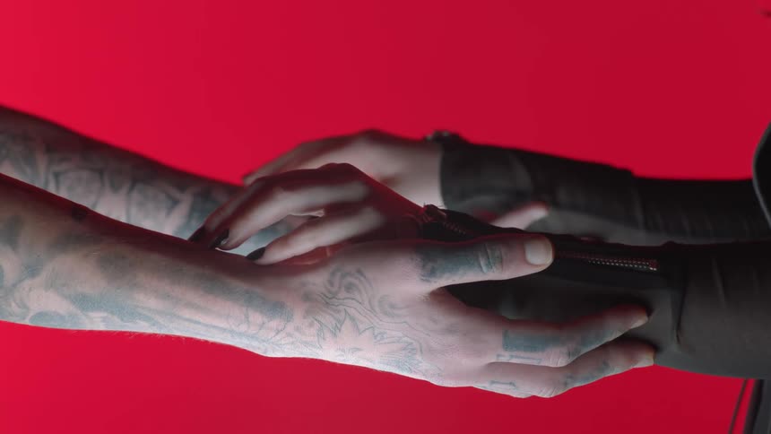 A man with tattooed arms holds out his hands for his female companion to caress and hold