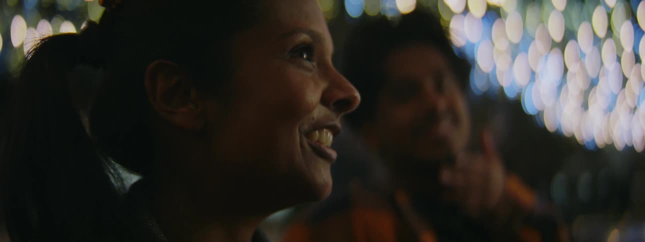 A man and woman stand under lights outside and talk
