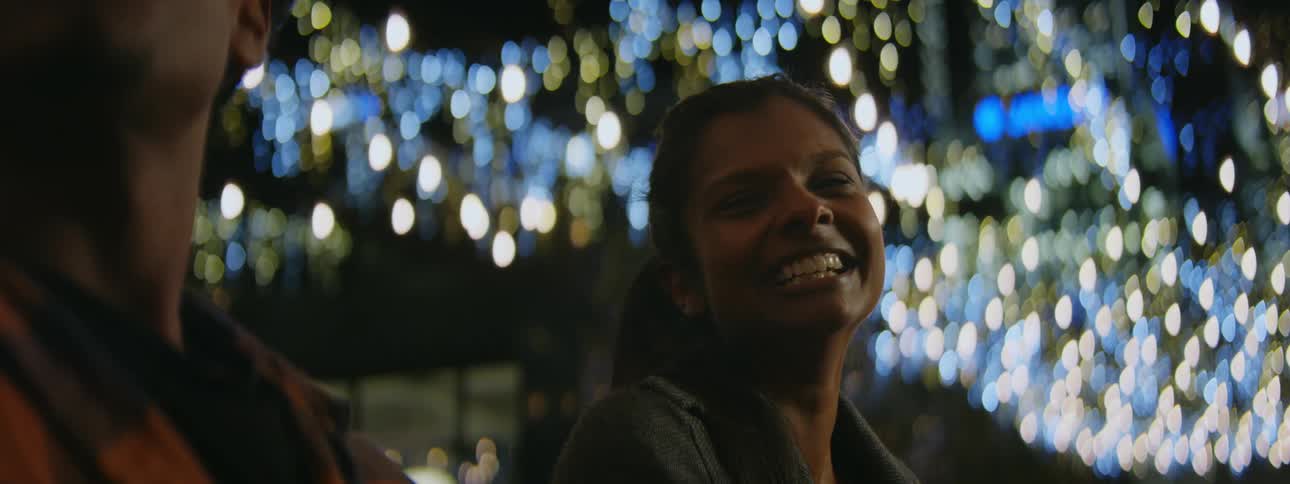 A woman smiles and laughs while listening to her male companion talk
