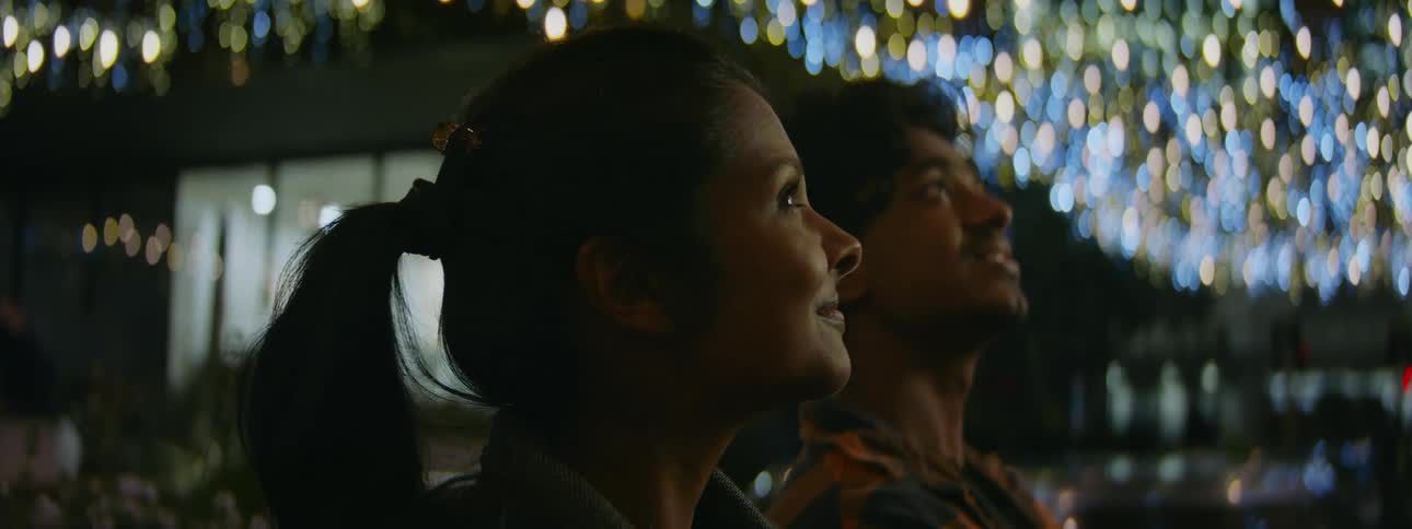 A man and woman outside look up at the sky as they talk and smile