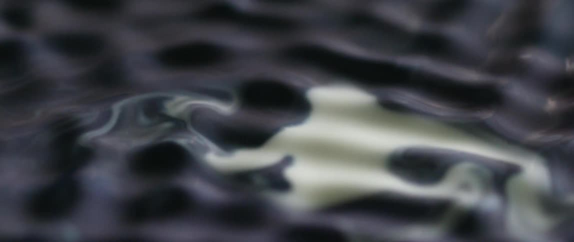 A black liquid with a patch of white in it undulates and begins to mix in the white