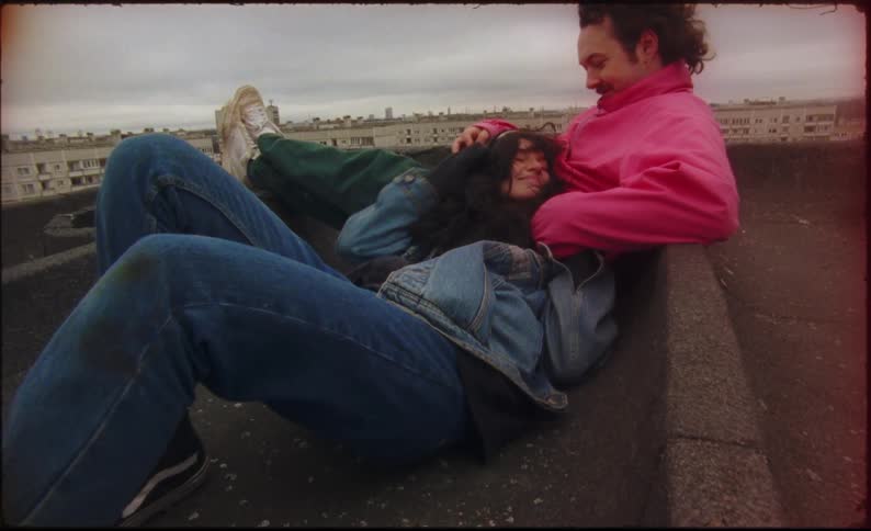 A man and woman are cuddled up on a rooftop in a city
