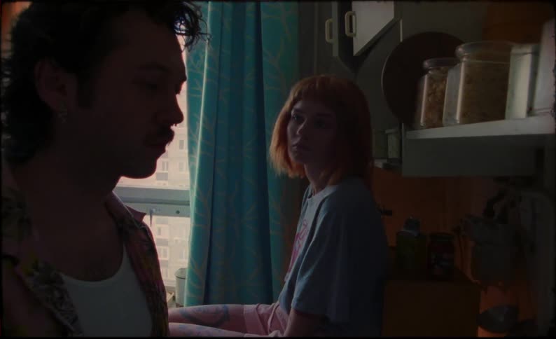 A woman sits on the kitchen counter and watches her boyfriend cook