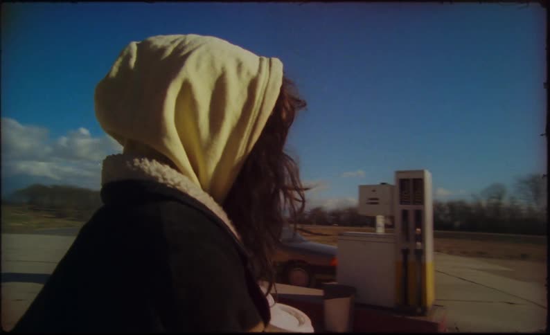 A woman is walking at a gas station in a rural area