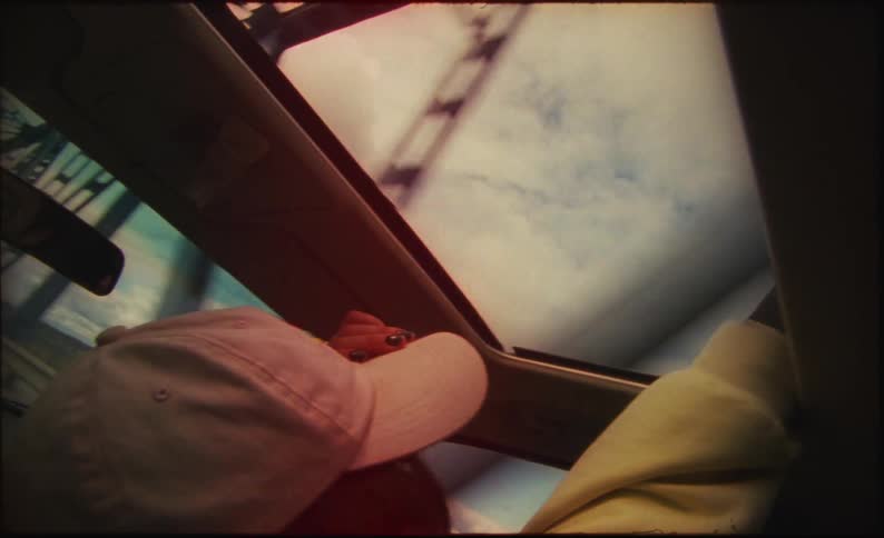Two people are traveling in an automobile and the girl in the passenger side sticks her hand out of the sunroof as they cross a bridge