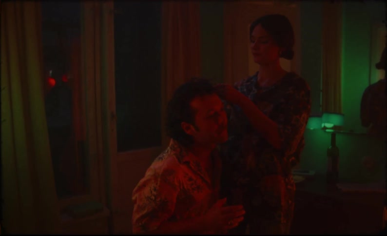Woman playfully cuts the hair of a man drinking and dancing on an apartment at night