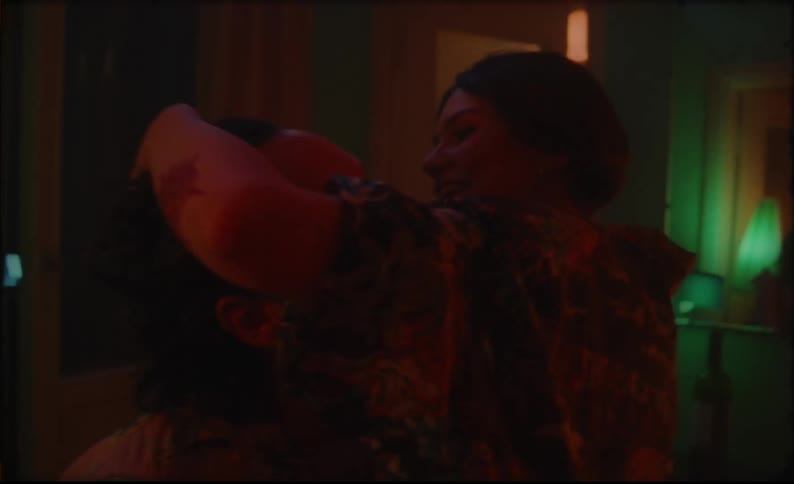 A woman cuts her boyfriends hair in a hotel room and climbs in his lap to kiss him